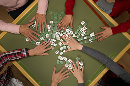 Hands sorting mahjong tiles on table top