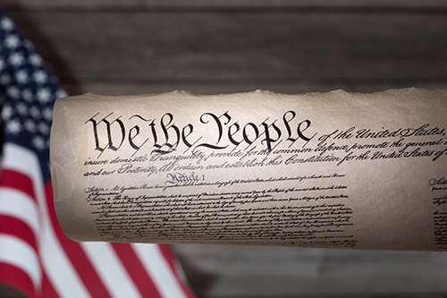 American Flag on left and scrolled US Constitution in center with the words We the People