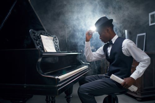 Black man in vest, bow tie and bowler hat sitting at grand piano