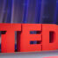 Red logo for TED talks on a stage in front of a blue curtain