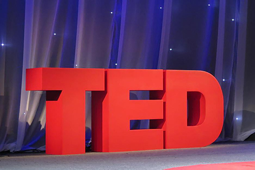 Red logo for TED talks on a stage in front of a blue curtain