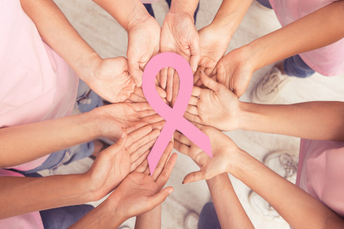 Pink Breast Cancer ribbon lays atop a circle of hands