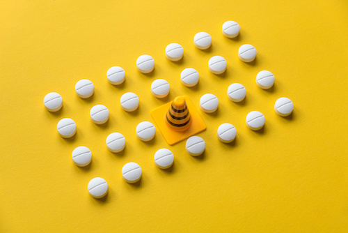 A row of white medical pills on yellow background with one missing spot in the middle fill by safety cone.