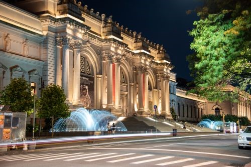 Photo of the outside of the Metropolitan Museum of Art at night with fountains in front
