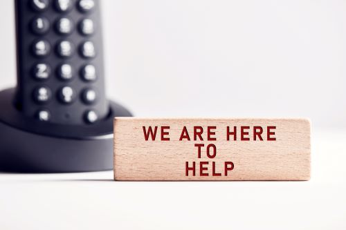 A sign saying "We are here to help" next to a telephone