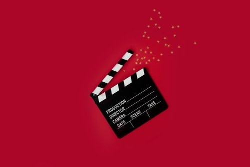 Open clapperboard with gold stars confetti on a red background.