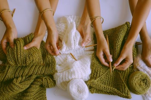Photo of pairs of hands with knitting needles working on green and white items