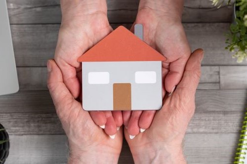 two sets of hands together holding a smal house.