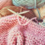 Up close photo of knitting needles and a pink knitted product
