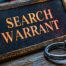 Plaque with the words "search warrant" on it, alongisde handcuffs