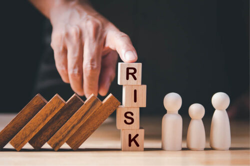 Scrabble letters forming the word "risk" with books and people like figures beside