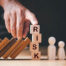 Scrabble letters forming the word "risk" with books and people like figures beside