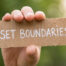 hand holding up cardboard sign that says "Set Boundaries"