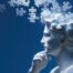 Sculpture of a man's head with puzzle pieces swirling around it.