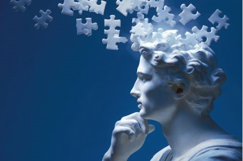 Sculpture of a man's head with puzzle pieces swirling around it.